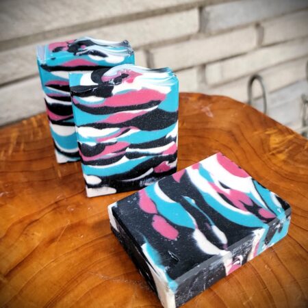 handmade bars of soap on a wood table. soap is coloured in black, teal, white and hot pink in a Miami tiger stripe like camouflage pattern