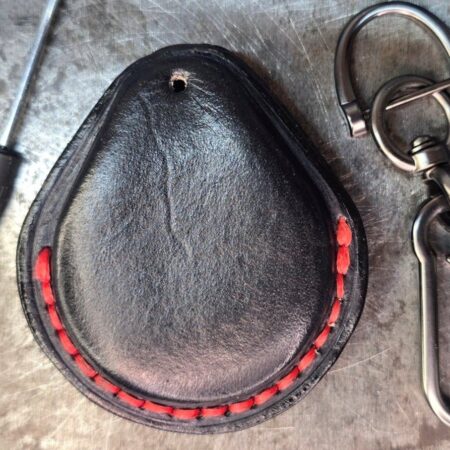 Back view of a black Harley Davidson key fob case with red stitching next to the stainless steel lobster clasp keychain and small screwdriver.
