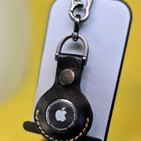 Black leather Apple AirTag case with orange stitching hanging from a lobster clasp keychain.
