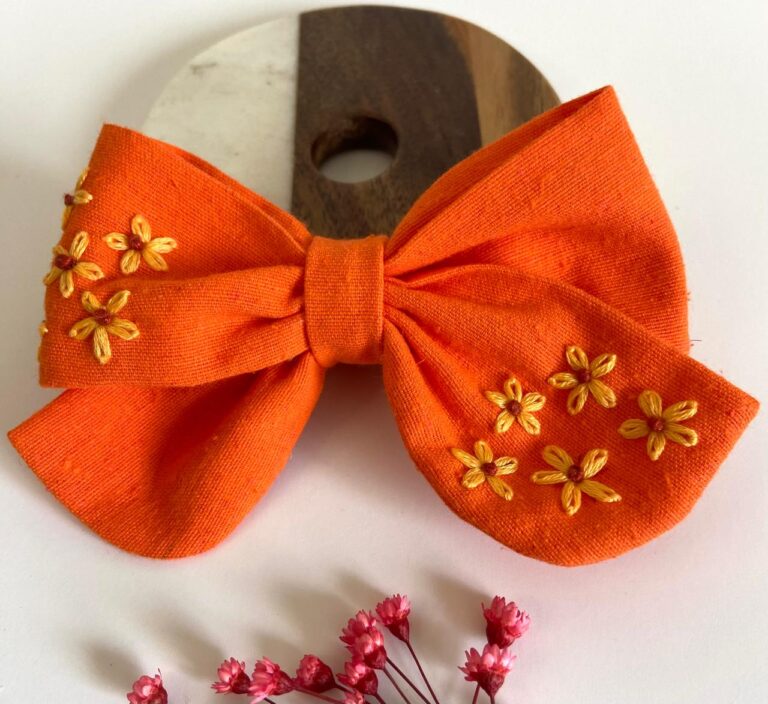 Hand-embroidered apricot linen bow with pastel floral details from Thread & Stitch Studio.