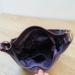 A Slouchy multi pockets eggplant color bag with iridescent hardware and decorative zipper tassels