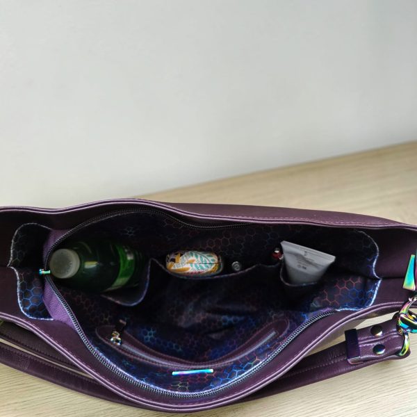 A Slouchy multi pockets eggplant color bag with iridescent hardware and decorative zipper tassels