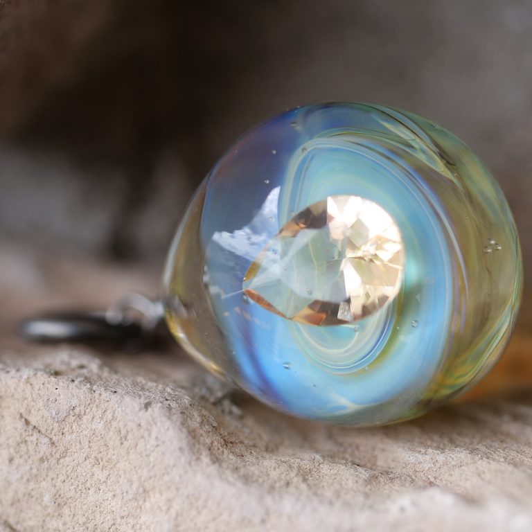 Close-up of a handmade blue glass pendant with a clear crystal inside